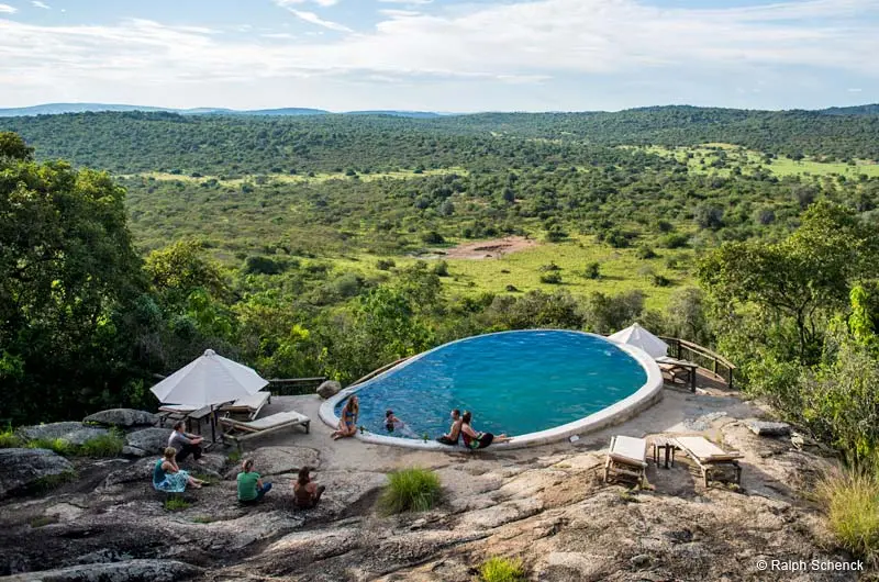 Personen sitzen am Pool und genießen die Aussicht auf die weite grüne Landschaft