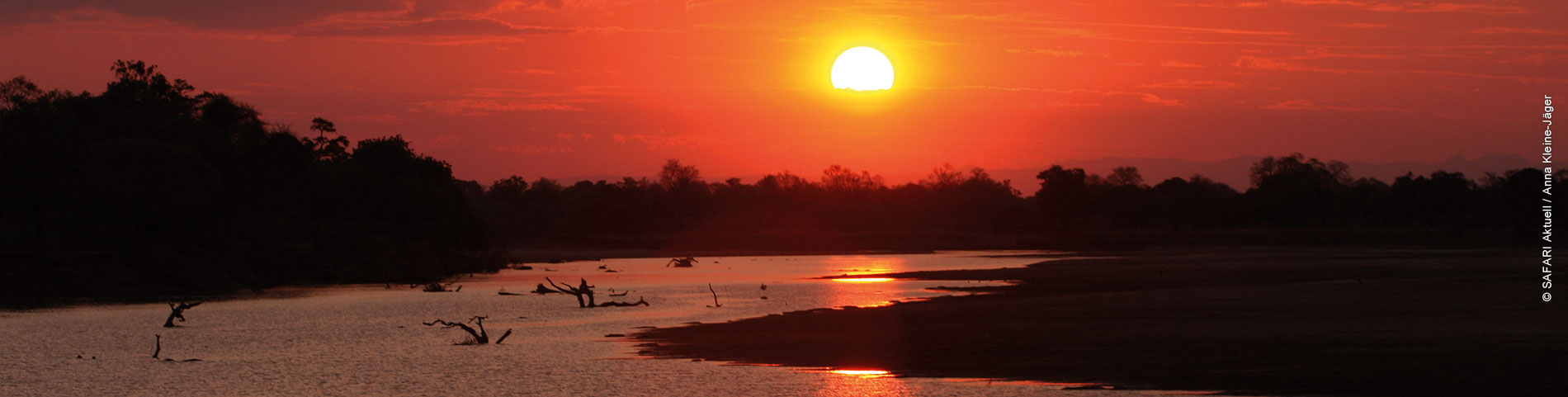 Roter Himmel mit Sonnenuntergang im Vordergrund Wasserstelle mit Silhouetten von Bäumen