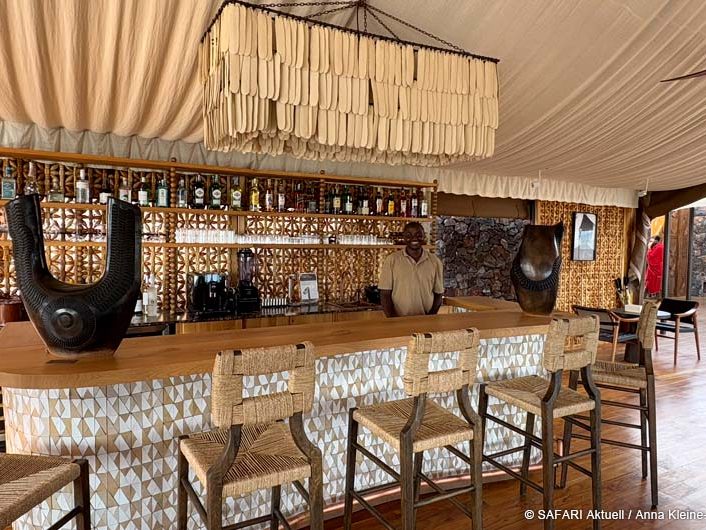 Bar mit Barhockern im Vordergrund. Hinter der Bar lächelt ein Mann.