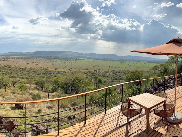 Panorama Motiv der Laba Grumeti Art Lodge. Große Terrasse mit Holzboden, Sitzgelegenheit unter Schirm und einer wunderschönen weiten Aussicht auf die Landschaft.