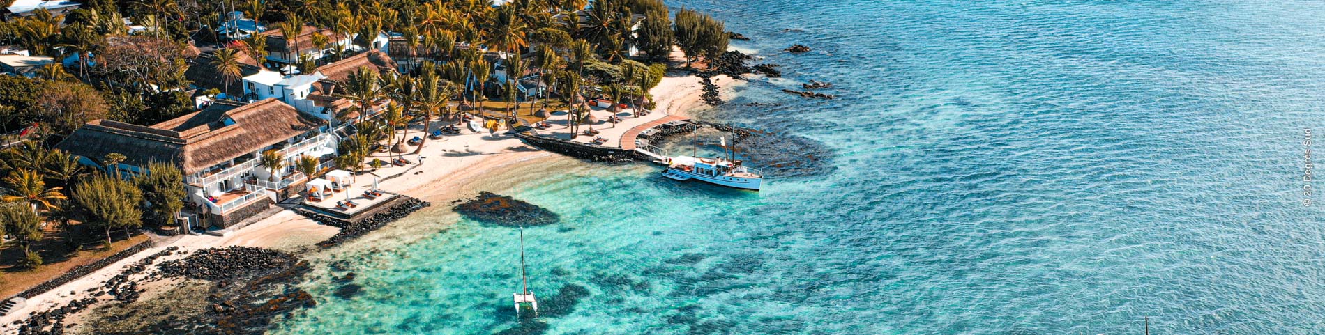 Kleine Insel mit Bäumen und Hotelanlage im azurblauen Meer